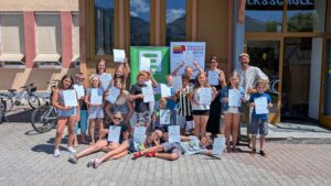Vor dem Schuleingang steht eine Gruppe von Volksschulkindern und zwei Erwachsenen mit Urkunden in den Händen.
